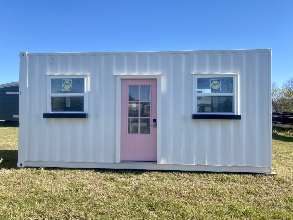 Shipping container tiny home with two windows and a pink front door